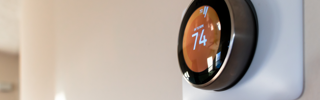 A round digital thermostat mounted on a wall displays the temperature set to 74 degrees.