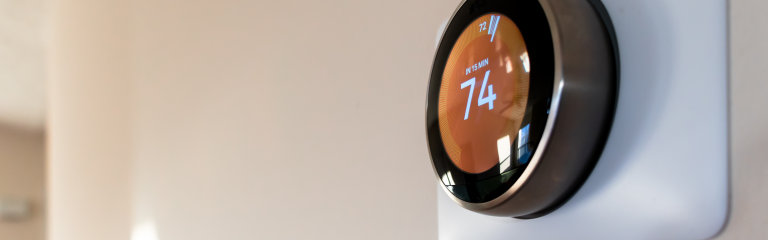 A round digital thermostat mounted on a wall displays the temperature set to 74 degrees.
