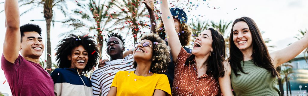 A diverse group of young adults celebrates with confetti and palm trees at a Valley Clean Energy Events gathering outdoors.