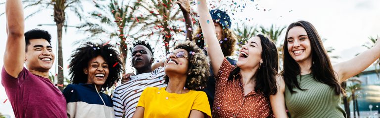 A diverse group of young adults celebrates with confetti and palm trees at a Valley Clean Energy Events gathering outdoors.
