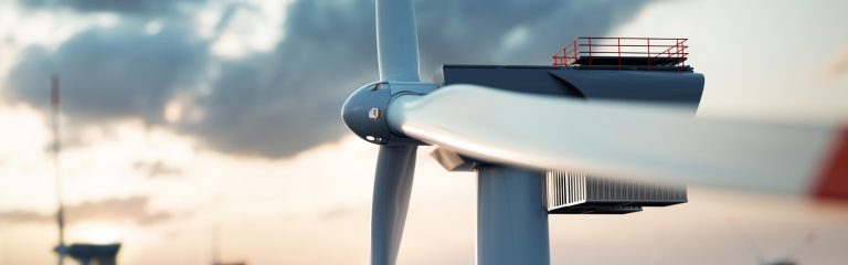 Close-up of a large wind turbine with blurred background and cloudy sky at sunset.
